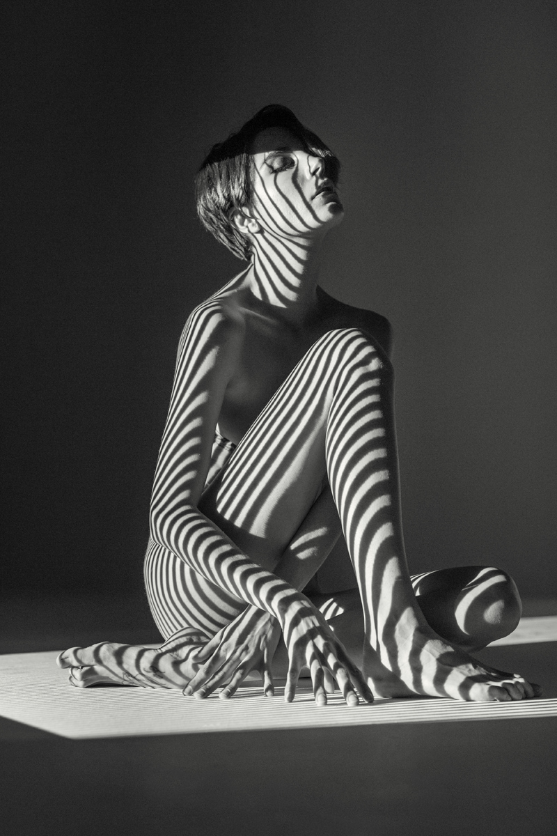 Roarie Yum seated nude with stripes projected on her naked body