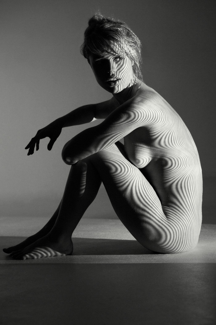nude woman in studio with projector light casting stipes
