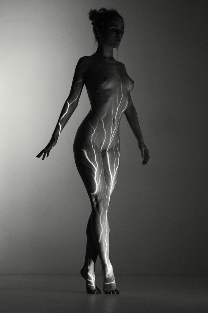 nude woman lit with a lightening stripe projector in a studio. Black and white art nude